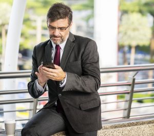 Homem interagindo com celular representa as redes sociais para corretores.